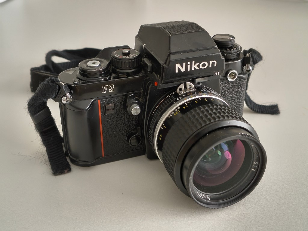 Close-up of a Nikon F3 camera with a lens, placed on a light surface.